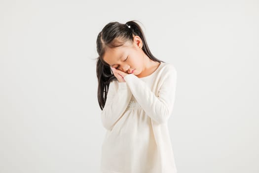 Portrait Asian young kid girl pretends emotions sleeping tired eyes closed dreaming with hands together near face, studio shot on white background, copy space, insomnia concept, kindergarten child