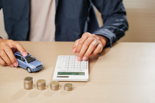 Hand on calculator calculating car loan near coin stacks and a car model. Perfect for financial, insurance, and tax planning, emphasizing new car sales, finance, and banking solutions. Car loan