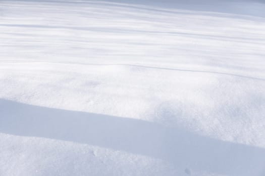 Wide soft snow cover with horizontal shadows stretching across the frame. Peaceful and minimalist representation of cold weather and winter atmosphere.