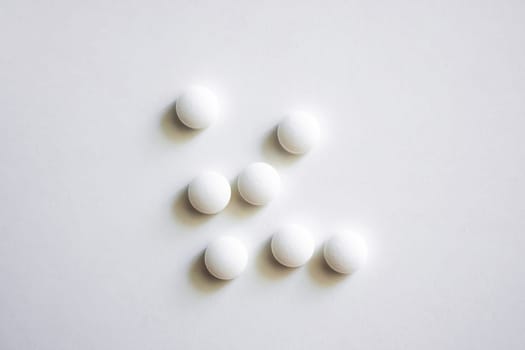 Close-up image of seven clean white round tablets on a bright surface, showing pharmaceutical purity, minimalism, and conceptual medicine dosage or treatment.