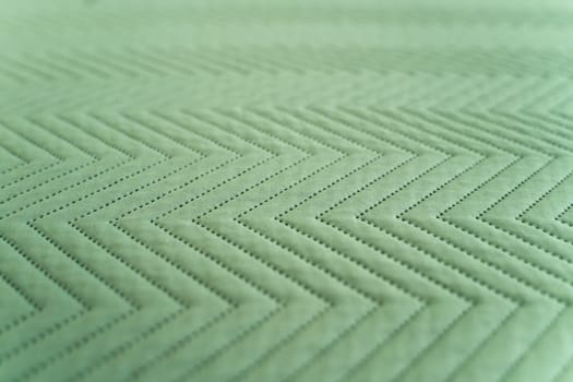 Textile surface in green color featuring regular zigzag stitching and punctured details forming a geometric fabric pattern, ideal for design, sewing, or textile concepts.