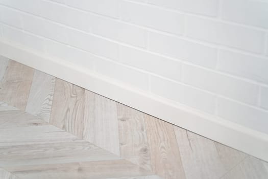 Perspective shot of a white painted brick wall and modern wood-patterned laminate floor, capturing clean lines and soft transitions in contemporary interior.
