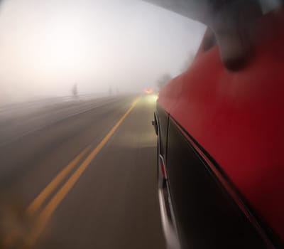 A blurry shot of a car driving down a foggy road. The car is red and the road is yellow