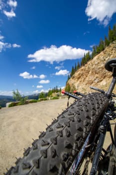 A mountain bike tire with a black and red design. The tire is on a dirt road with a blue sky in the background