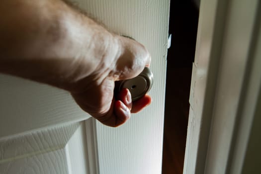 A hand is holding a door open. The door is white and the hand is visible. Scene is casual and relaxed