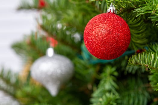 A red and silver ornament hangs on a Christmas tree. The tree is full of green leaves, and the ornaments are hanging from the branches