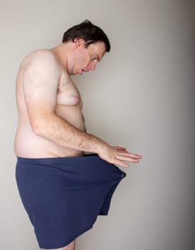 A man with a large belly is wearing a blue towel and is looking at the camera. Concept of vulnerability and discomfort, as the man is exposing a large part of his body