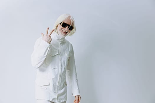 A trendy young individual dressed in an all white ensemble stands against a light backdrop, showcasing a peace sign with a smile, embodying a contemporary and positive lifestyle