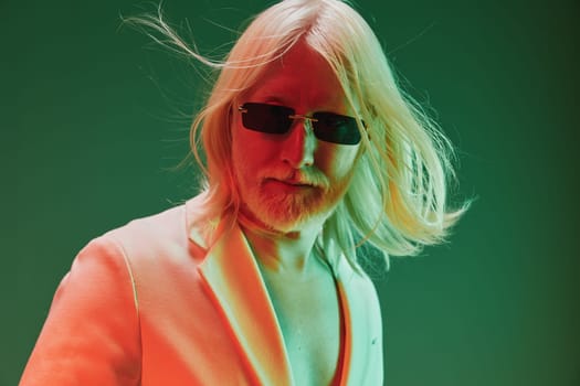 A striking image of a confident man with long blond hair and sunglasses, dressed in a sharp suit, set against a dynamic green and orange gradient background that enhances his stylish look