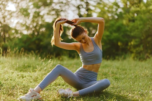 Young woman in blue sportswear stretching in a sunlit green park, demonstrating a dedication to fitness and a healthy lifestyle The vibrant, natural background enhances the sense of well being and c