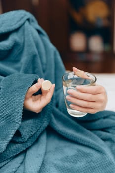 Woman in blue blanket with glass of water and pill bottle.