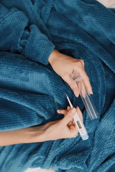Person laying on bed with blue blanket and bottle of nail polish beside their hand.