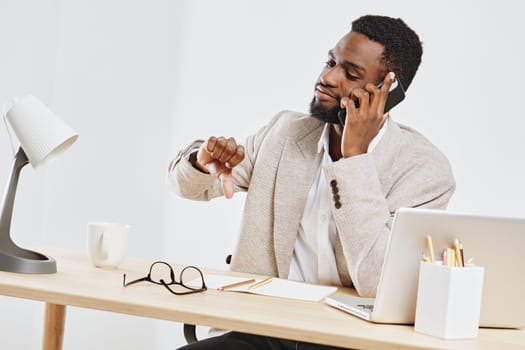Confident man in smart casual attire using mobile phone, seated at an organized desk with laptop, glasses, and stationery. Bright office environment, focused expression, productivity, modern professional atmosphere.