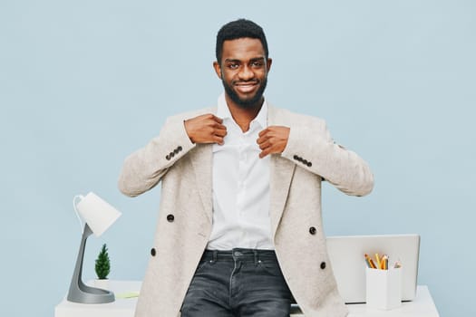 Confident smiling man in stylish beige blazer and white shirt standing at desk in contemporary office space with ergonomic chair, desk accessories, and sensor lighting. Bright, professional atmosphere, young professional lifestyle.