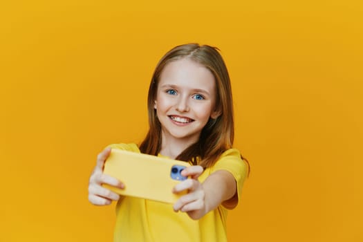 A joyful girl taking a selfie with her yellow smartphone, dressed in a matching yellow shirt Bright yellow background enhances the cheerful and playful atmosphere