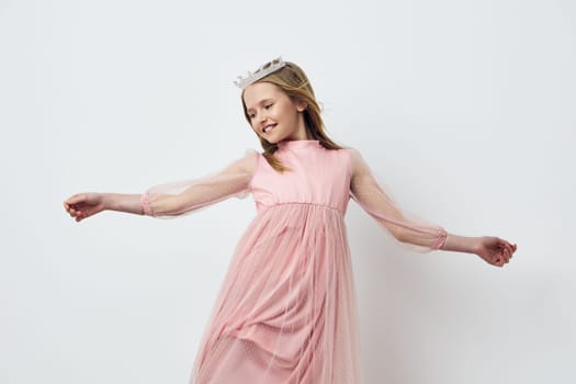 A joyful young girl in a pink dress and crown is dancing gracefully against a soft white background, embodying the themes of innocence and childhood joy in a spring setting