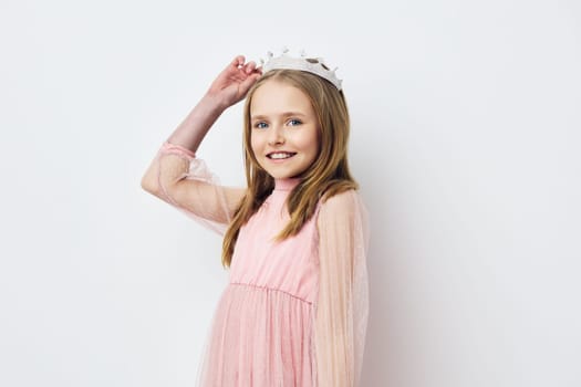 A cheerful young girl in a pink dress and crown, exuding happiness and innocence, poses against a light background, embodying joy and playful spirit in a child friendly concept