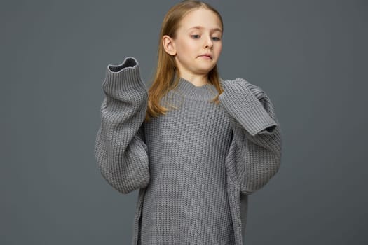 A young girl displaying a relaxed pose in an oversized gray sweater, radiating confidence and comfort The neutral gray background complements the fashion aesthetic, perfect for lifestyle and children s clothing themes