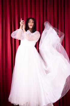 Asian woman posing in a white wedding dress and had black hair inside the red curtain room