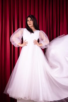 Asian woman posing in a white wedding dress and had black hair inside the red curtain room