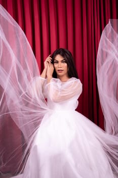 Elegance Asian woman wearing a wedding dress with flying fabric around her in front of the red curtain inside the studio