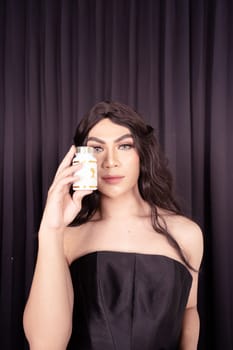 Beautiful Woman holding skincare in her hand while wearing a black dress with black hair in front of the black curtain