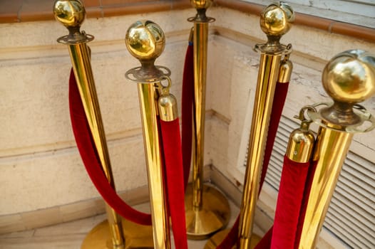 Gold colored metal stanchions with red velvet rope for crowd control. A group of red velvet ropes and gold poles on the street, waiting to be installed near the hotel building.