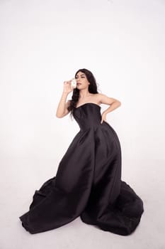 glamor woman holding a skincare jar in her hands with black hair and dress inside the white room