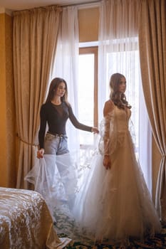 A bridesmaid helps a young bride get ready for her wedding day. A bridesmaid adjusts an elegant bride's lace dress. The morning of the wedding day.