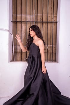 Sad Asian woman standing in front of the brown wooden window while wearing a black dress inside the studio