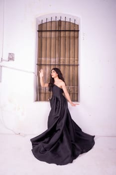 Sad Asian woman standing in front of the brown wooden window while wearing a black dress inside the studio