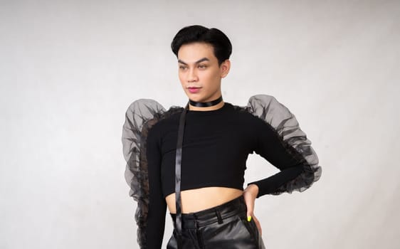 A transgender man poses in a black dress with an elegance face and black hair inside the white studio