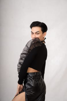 A transgender man poses in a black dress with an elegance face and black hair inside the white studio