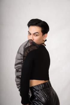 A transgender man poses in a black dress with an elegance face and black hair inside the white studio