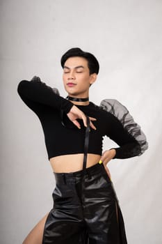 A transgender man poses in a black dress with an elegance face and black hair inside the white studio