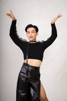 Portrait of a feminine man in black dress and black hair while wearing makeup inside the white studio