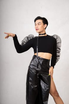 Portrait of a feminine man in black dress and black hair while wearing makeup inside the white studio