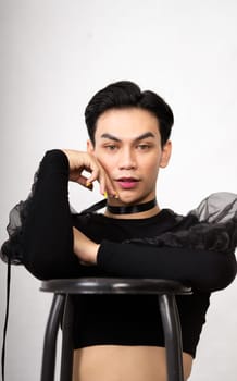 beautiful Asian man posing with the chair while wearing a black costume and makeup inside the white studio