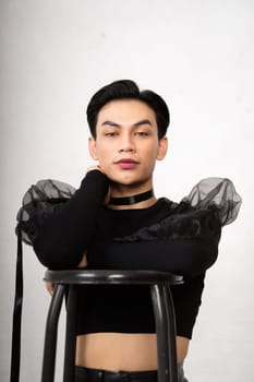 beautiful Asian man posing with the chair while wearing a black costume and makeup inside the white studio