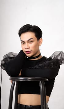 beautiful Asian man posing with the chair while wearing a black costume and makeup inside the white studio