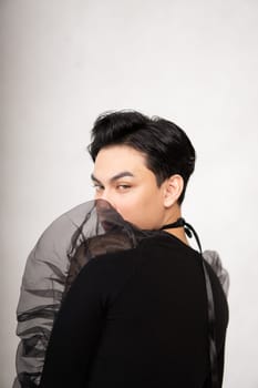 Asian man poses in a black costume while wearing makeup and black hair inside the studio
