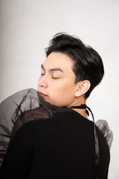 Asian man poses in a black costume while wearing makeup and black hair inside the studio