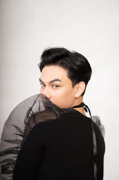Asian man poses in a black costume while wearing makeup and black hair inside the studio