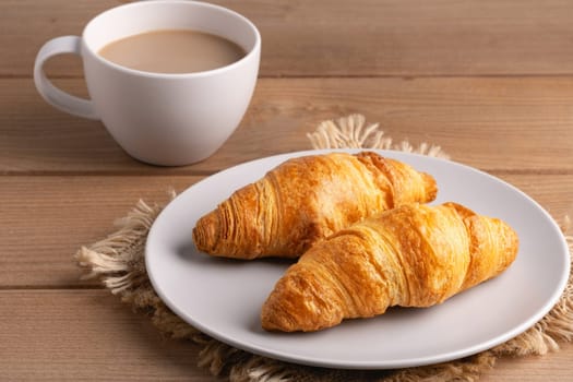 Freshly baked croissants served with a hot cup of coffee on a wooden table in a cozy setting,