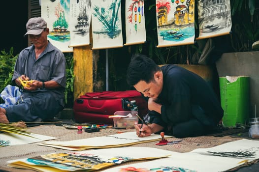 Asian men Vietnamese street artist painter and craftsman work on the streets of an ancient city in Hoi An in Asia. Hoi An, Vietnam - December 1, 2024