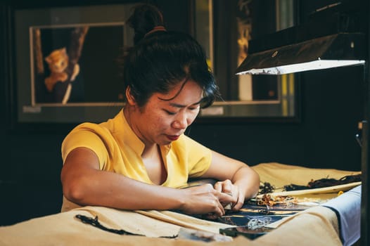 Vietnamese female embroiderer embroiders a silk painting in a workshop in the old town in Hoi An city in Vietnam in Asia. Hoi An, Vietnam - December 1, 2024