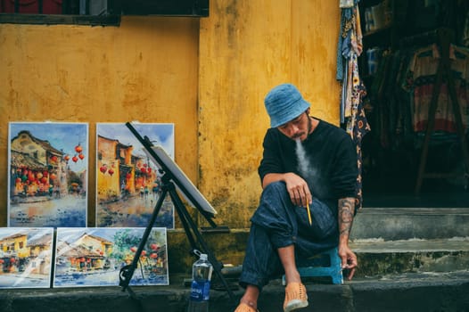Asian young male Vietnamese street artist painter drawing on streets of an ancient town in Hoi An in Asia. Hoi An, Vietnam - December 1, 2024