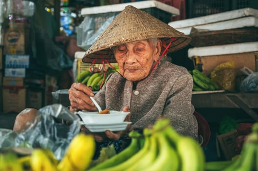 Old elderly Vietnamese woman selling fruit at an Asian food market on street in Hoi An in Vietnam in Asia. Hoi An, Vietnam - December 1, 2024