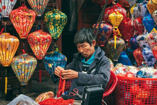Asian man artisan craftsman makes Vietnamese silk lanterns in market at ancient town in Hoi An city in Vietnam. Hoi An, Vietnam - December 1, 2024