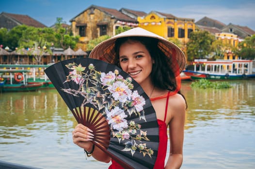 happy young female tourist traveler in a Vietnamese hat with a fan on a bridge in Hoi An in Vietnam in Asia